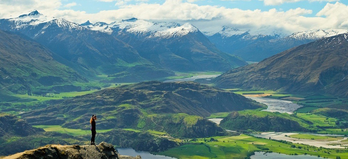 tourist standing on mountain in New Zealand with green hills below
